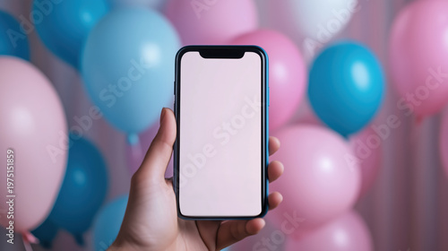 Hand holding smartphone with blank screen amidst blue and pink balloons