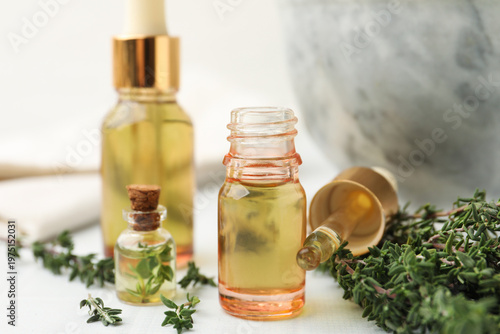 Thyme essential oil and fresh herbs on white table, closeup