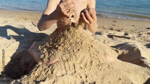 Child joyfully digging, shaping, and tossing sand while sitting on a bright seaside shore, enjoying playful summer fun and carefree moments under the warm sunlight near the gentle ocean waves