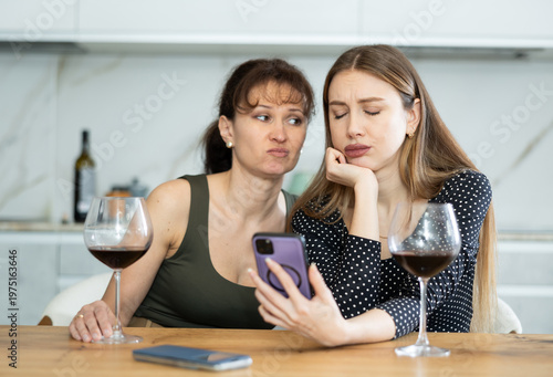 Obraz na płótnie Two sad middle-aged women looking at the phone display while sitting at the tabl