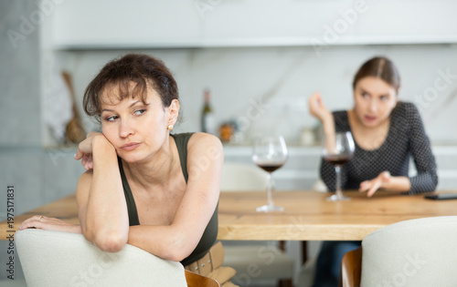 Offended middle-aged woman sitting in the kitchen while other woman talking angrily to her