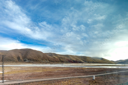 Expansive mountain landscape under a dramatic cloudy sky. A river flows across the valley with a road cutting through the scene, ideal for travel, adventure, freedom, solitude, and nature concepts