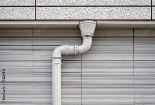 White drainpipe against a gray wall of a building exterior.