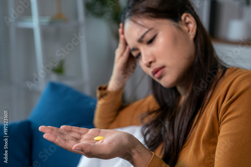 Young woman feeling sick holding pill and touching forehead at home