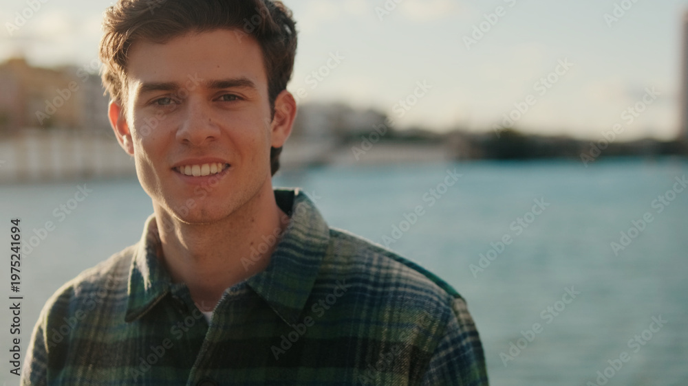 Fototapeta premium Smiling Young Man By Riverbank At Sunset