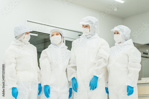 Canvas Print Male and female staff working in a manufacturing plant, wearing protective suits and cleanroom wear