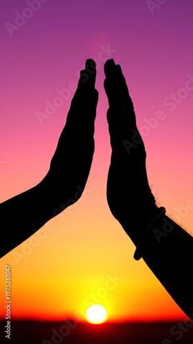 A silhouette of two hands touching against a vibrant sunset sky during a peaceful evening