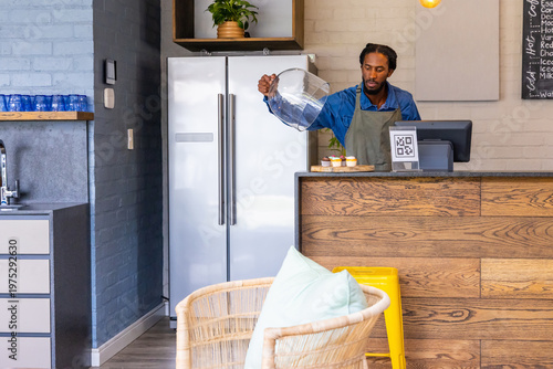 African-American man 30s pouring from pitcher behind wood counter at cafe with QR sign, copy space