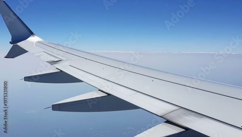 Airplane wing seen from inside cabin window flying above clouds during daytime flight