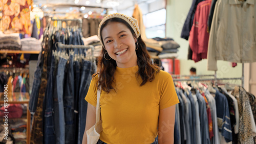 Young teen Gen Z asia female happy smile looking at camera at zero waste eco go green buy second hand sale store flea market mall thrift old used vintage fabric retro style. Woman people enjoy shop.