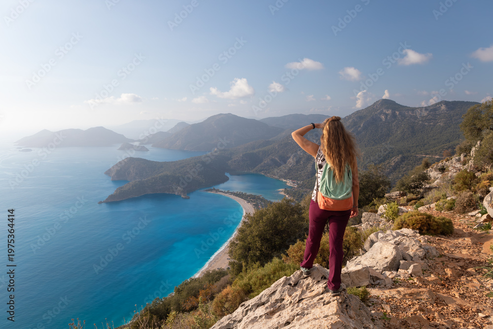 Fototapeta premium Young woman looking at Oludeniz beach, blue lagoon with clear bright turquoise water, Lycia coast. Summer day walk by Lycian way at family vacation in Mediterranean Sea, Fethye, Antalya region, Turkey