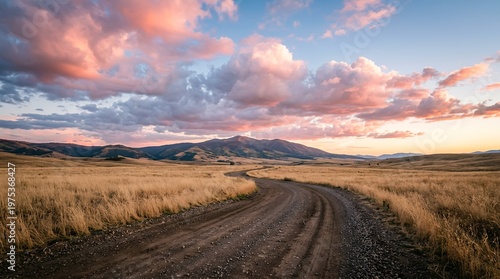 Rural road through golden grassland with dramatic cloudy sky and mountain horizon