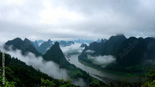 Panoramic view of misty mountains and a river. Lush green, clouds, moody day