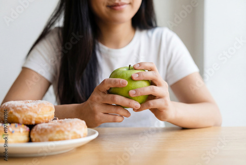 Woman choosing a healthy green apple over a plate of sweet donuts