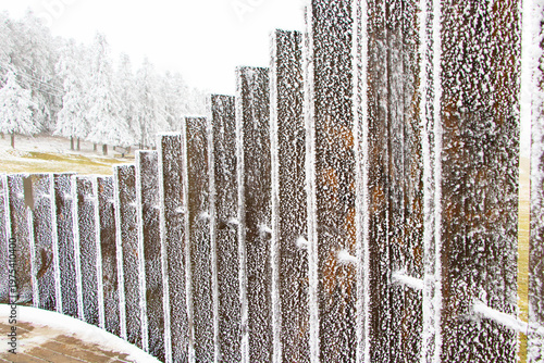 Snow attached wooden brown fence pattern in winter frosty texture repeating lines creating minimal moody composition. Cold serene scene soft snowfall. Seasonal concepts nature is background.