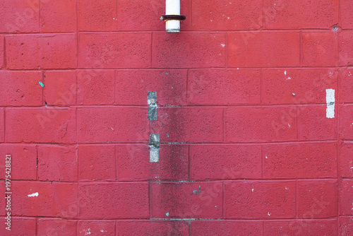 red painted concrete block wall with vertical water stain and white pipe