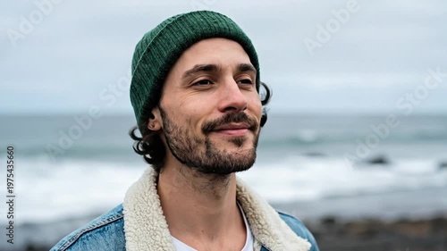 Young man with a beard and beanie enjoying the fresh air on an overcast beach by the ocean