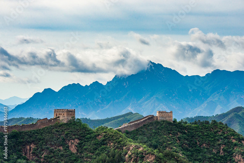 Aerial view of Jinshanling Great Wall of China stretching across mountain ridges under blue sky and dramatic afternoon clouds. 