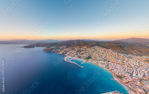 Фотография Kusadasi, Turkey - July 4, 2025: Aerial panorama of mountains, bay, yacht marina, beaches, promenade, and city in sunset glow