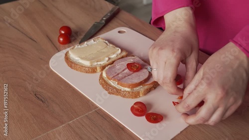 A woman stuffs a sandwich with sausage and tomatoes. Cooking at home.