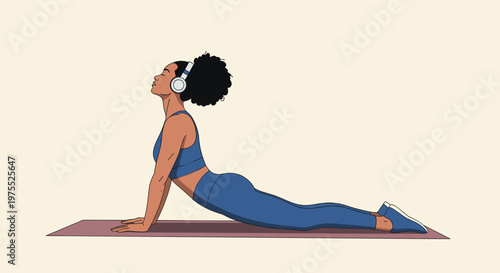 Athletic black woman in a blue tracksuit performs the cobra yoga pose while listening to music with white headphones for a mindful workout.