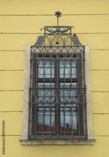 Old brown window with ornate wrought iron bars on yellow wall closeup