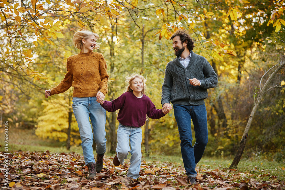 Naklejka premium In a vibrant autumn park, a family runs through fallen leaves, holding hands and laughing together. They enjoy each other's company, soaking in the beauty of the season.