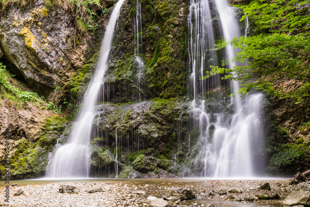 Obraz premium Scenic waterfall in lush green forest with rocky riverbed in summer morning in Bavaria Germany 