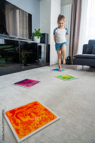 Little girl stepping and jumping on colorful sensory gel mats placed on floor at home. Sensory development, autism support and occupational therapy activity concept.