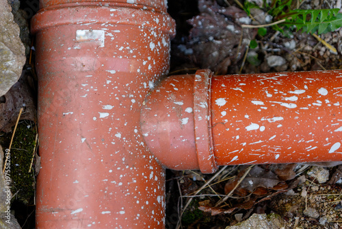Red t-joint drainage pipe with paint splatters and construction debris