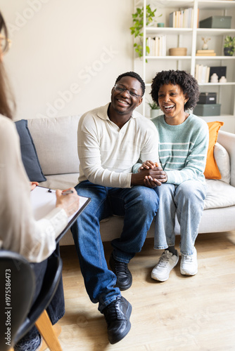 Happy couple holding hands talking with psychologist on therapy session
