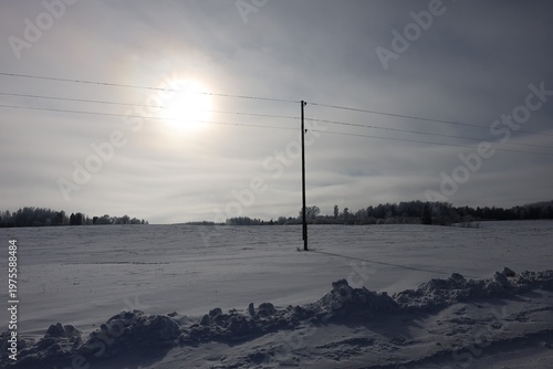 cold snowy field with sun halo power lines and distant forest silhouette