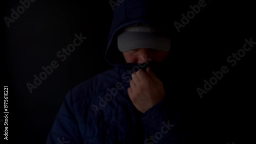 Dark hooded figure masks face, hand covers mouth. Silent, tense, secretive gesture suggests concealment or fear. Ideal for suspense, mystery, or privacy-themed visuals