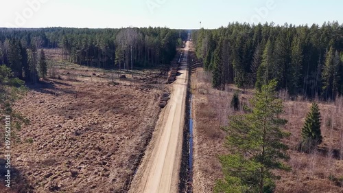 Aerial view of a dirt road cutting through a forested area with cleared land on both sides, showcasing the transition from dense trees to open terrain