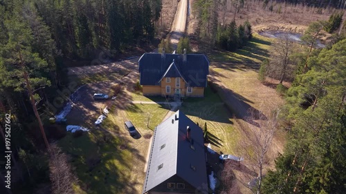 Aerial view of a large yellow house surrounded by green trees and a gravel road leading to the property, showcasing the natural landscape in a serene rural setting