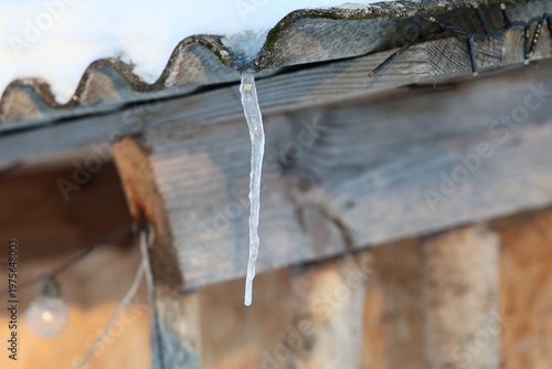 frozen water drop forming icicle on rustic roof with winter background