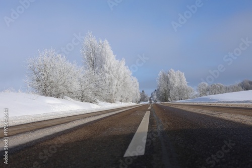 asphalt road in winter with snowbanks frost covered trees and blue sky