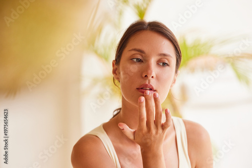 Foto Lip care woman gently touching her lips with fingertip, eyes half-closed in a serene expression, with tropical palm bokeh in background