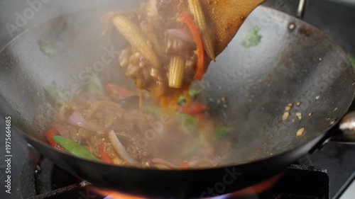 Stir-frying vegetables and meat in a hot wok, close-up of a wooden spoon tossing fresh ingredients over an open flame for healthy Asian-style cooking.