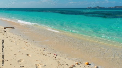 Turquoise ocean waves washing over a pristine white sand beach, tropical island coastline with clear blue water and sunny sky.