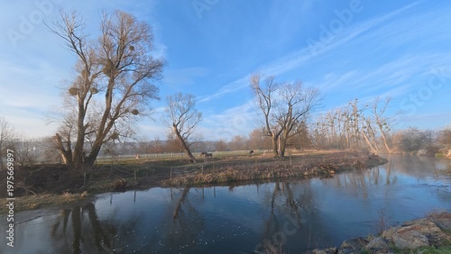 Small river weir with flowing water creating a gentle cascade. The scene captures movement, texture of water, and a calm natural atmosphere in a countryside setting.