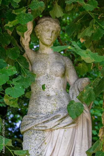 Classical stone statue hidden among green leaves