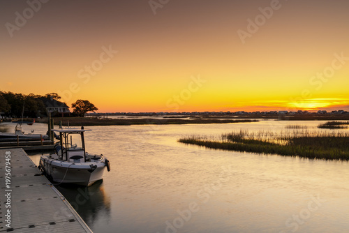sunrise over the salt marsh of Murrells Inlet with a boat and the waterfront boardwalk in the foreground