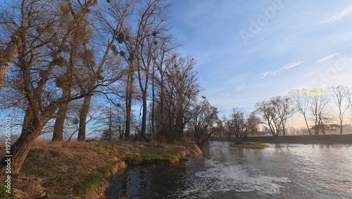 Small river weir with flowing water creating a gentle cascade. The scene captures movement, texture of water, and a calm natural atmosphere in a countryside setting.