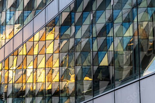 Modern glass building facade with diagonal geometry and warm urban reflection creating dynamic architectural pattern in close detail