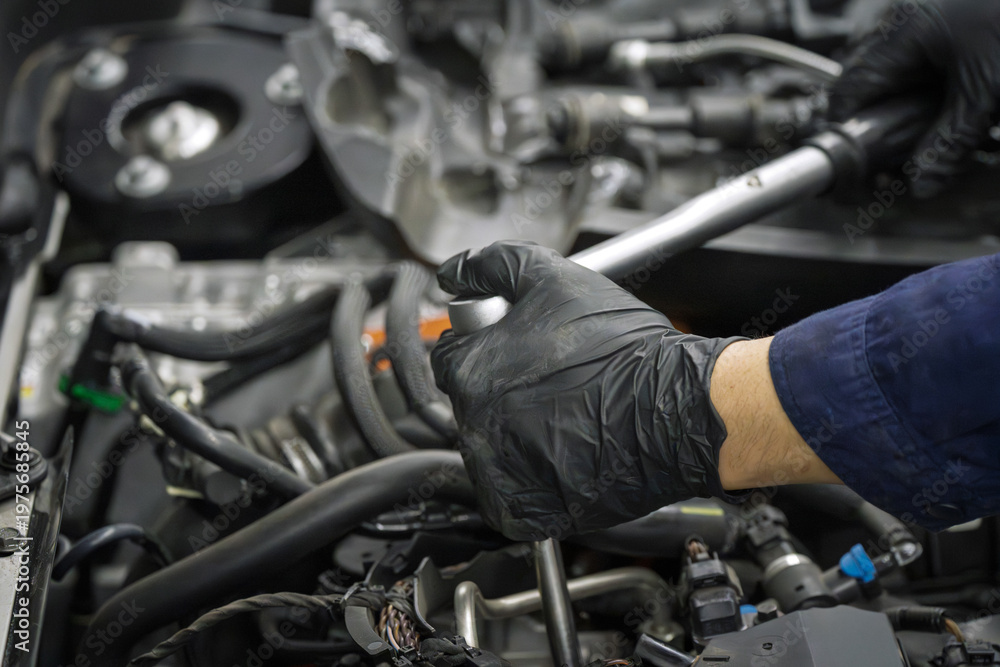 Fototapeta premium Mechanic in black gloves repairs car engine with wrench