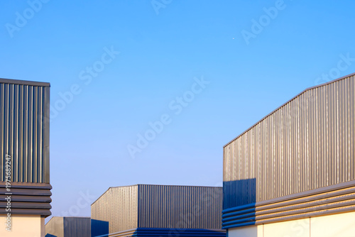 Group of modern industrial warehouse factory buildings with corrugated metal siding under blue sky. Concept of logistics, storage facility, and manufacturing plant exterior