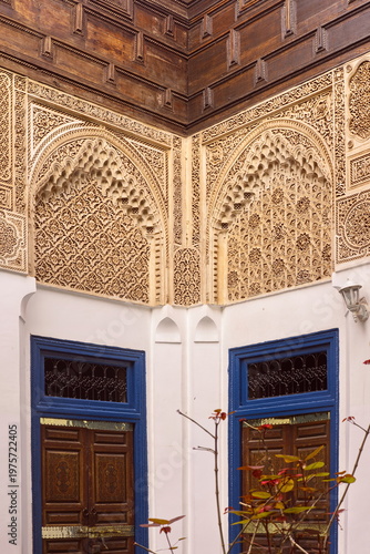 Richly carved stucco and wood corner wall above brass-plated, floral-painted, angled old wooden doors, Bahia Palace-Small Riad. Marrakesh-Morocco-265