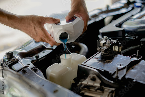  man's hands are pouring coolant into the car's cooling system. Car maintenance concepts.