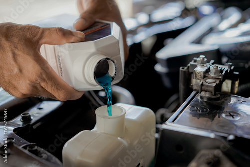  close-up  of a mechanic's hands filling or pouring coolant into a car's engine system. Car radiator maintenance